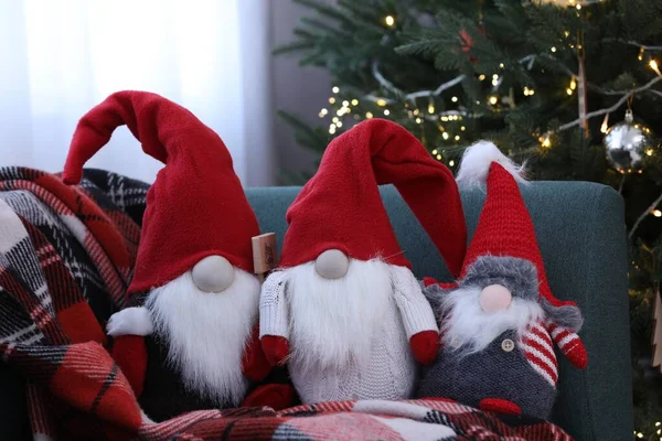 Funny decorative gnomes on sofa near Christmas tree