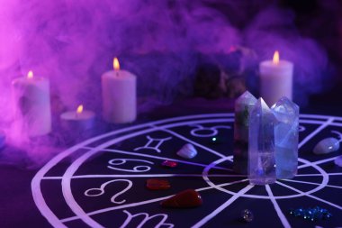 Zodyak işaretleri için doğal taşlar, astroloji çizelgesi ve siyah masada yanan mumlar. Renk tonu etkisi
