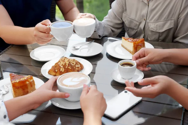 Friends drinking coffee at wooden table in outdoor cafe, closeup