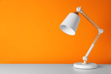 Turuncu duvarın yanındaki beyaz masada modern masa lambası, metin için alan