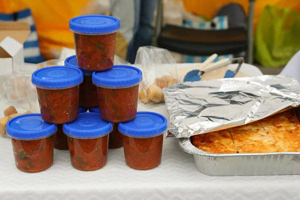 Volunteer food distribution. Containers with tasty adjika sauce near pie served on table outdoors