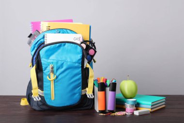 Children's backpack and different school stationery on wooden table against grey background