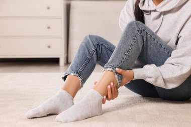 Woman suffering from leg pain on floor at home, closeup