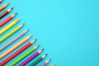 Açık mavi arka planda renkli ahşap kalemler, düz bir zemin. Metin için boşluk
