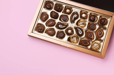 Box of delicious chocolate candies on pink background, top view. Space for text