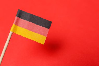 Small paper flag of Germany on red background, closeup. Space for text