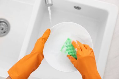 Günümüz mutfağında lavabonun üstündeki tabağı yıkayan kadın.