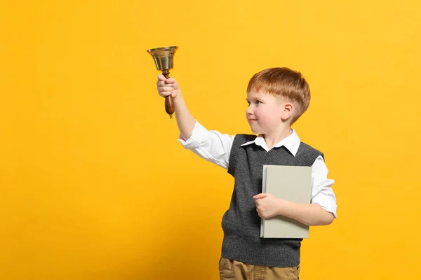 Pupil with school bell and book on orange background. Space for text