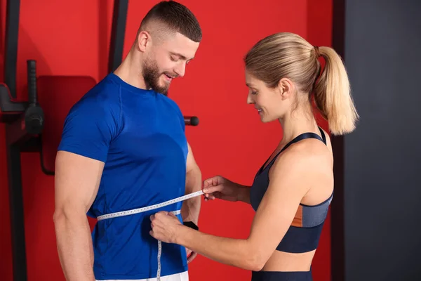 Trainer measuring man`s waist with tape in gym