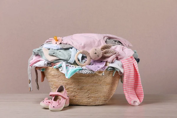 Laundry basket with baby clothes and shoes on wooden table