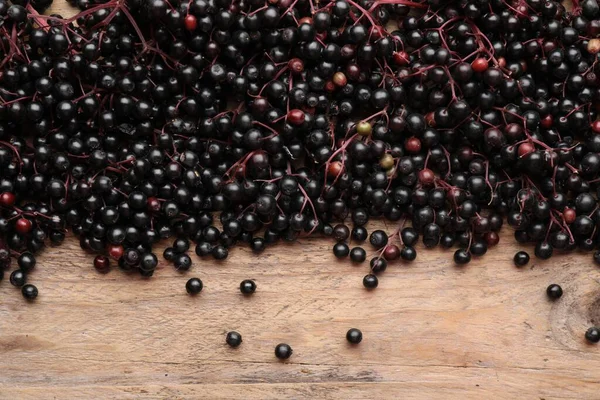 Black elderberries (Sambucus) on wooden table, flat lay. Space for text
