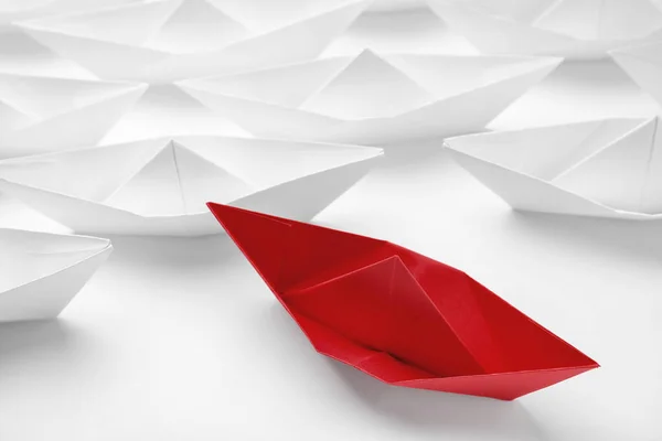 Red paper boat floating away from others on white background, closeup. Uniqueness concept