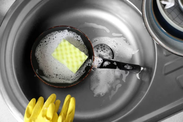 Dirty frying pan with sponge in kitchen sink, above view