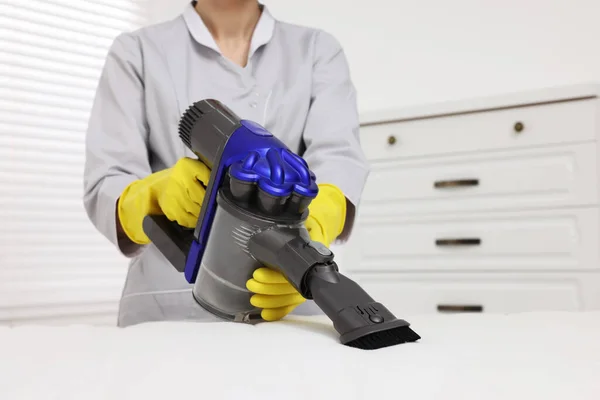 Woman in gloves disinfecting mattress with vacuum cleaner indoors, closeup. Space for text