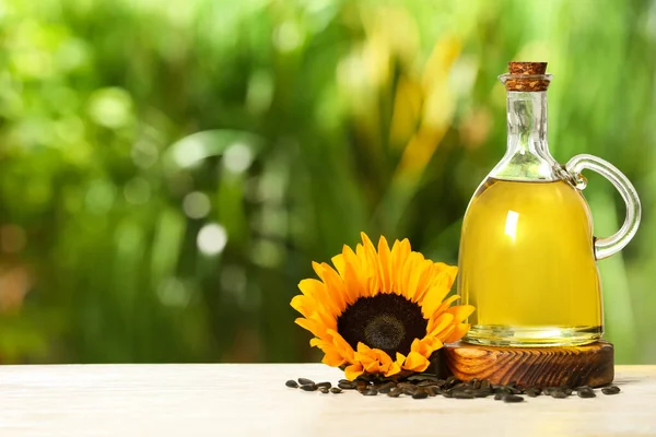 Sunflower cooking oil, seeds and yellow flower on white wooden table outdoors, space for text