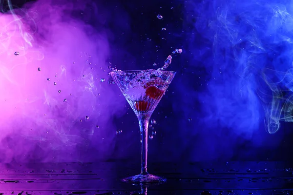 Martini splashing out of glass on table in neon lights