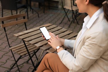 Woman using smartphone at table in cafe outdoors, closeup