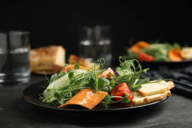 Delicious vegetable salad with microgreens served on black table