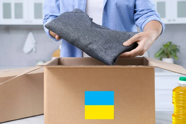 Humanitarian aid for Ukraine. Man putting clothes in donation box at white table indoors, closeup