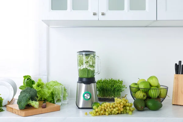 Blender with delicious smoothie and ingredients in kitchen