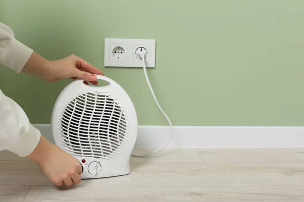 Woman turning on electric fan heater indoors, closeup. Space for text