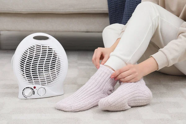 Woman warming near modern electric fan heater on floor indoors, closeup