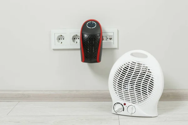Modern electric compact and fan heaters indoors, space for text