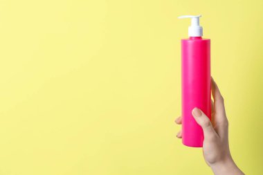 Woman holding spray bottle with hair thermal protection against pale yellow background, closeup. Space for text
