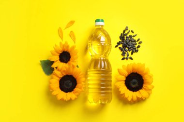Bottle of cooking oil, sunflowers and seeds on yellow background, flat lay