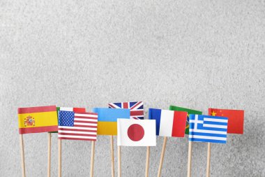 Many small paper flags of different countries on grey textured table, flat lay. Space for text