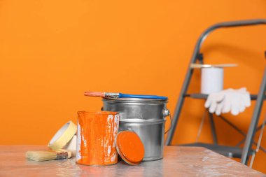 Can with paint, brush and renovation equipment on table against orange background