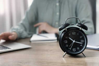Black alarm clock and woman working on laptop at table, closeup. Space for text