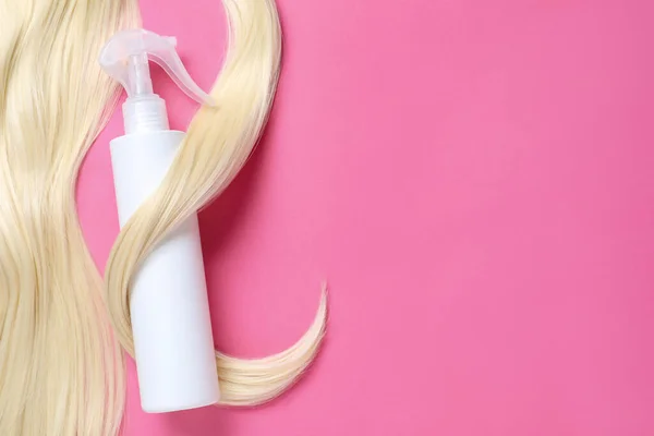 Spray bottle with thermal protection and lock of blonde hair on pink background, flat lay. Space for text