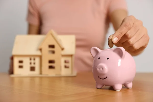 Woman Putting Money Piggy Bank Holding House Model Wooden Table — Foto de Stock