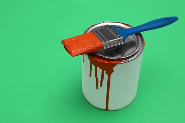 Can of orange paint and brush on green background. Space for text