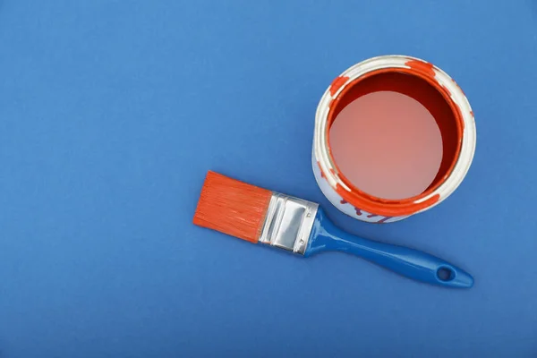 Can of orange paint and brush on blue background, top view. Space for text