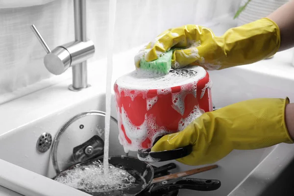 Woman washing pot in kitchen sink, closeup