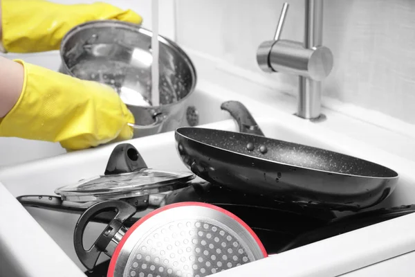 Woman washing pot in kitchen sink, focus on dirty kitchenware