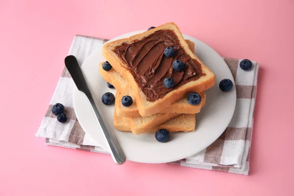 Tasty toast with chocolate paste and blueberries on pink table