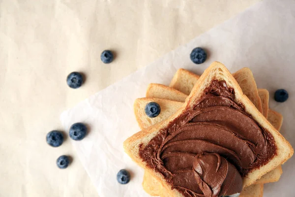 Tasty toast with chocolate paste and blueberries on parchment paper, flat lay