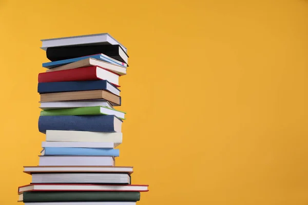 Stack of hardcover books on orange background. Space for text