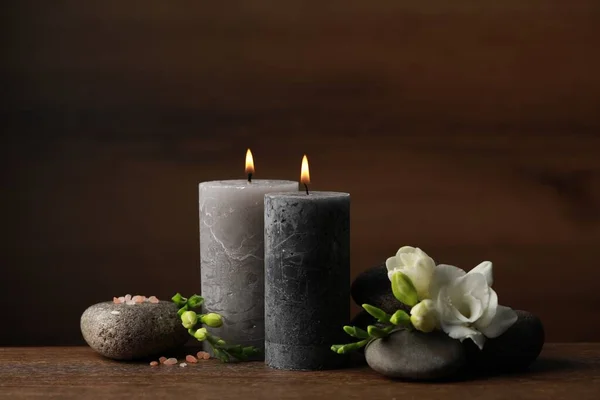 Beautiful composition with burning candles, spa stones and flowers on wooden table