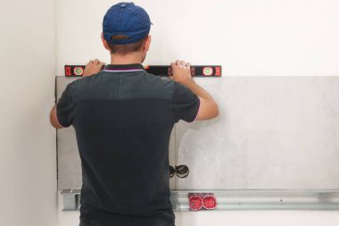 Worker installing wall tiles indoors, back view