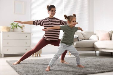 Young mother and her daughter practicing yoga together at home