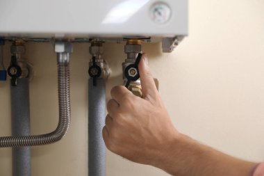 Man turning on valve of gas boiler, closeup