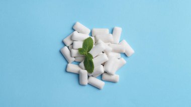 Tasty chewing gums and mint leaves on light blue background, flat lay