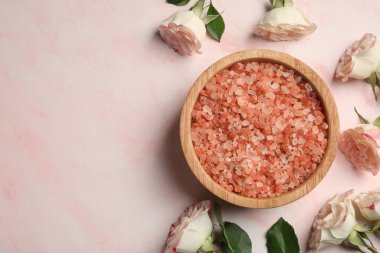 Aromatic sea salt and beautiful roses on pink marble table, flat lay. Space for text