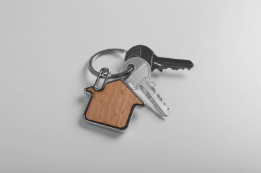 Keys with trinket in shape of house on white background. Real estate agent services