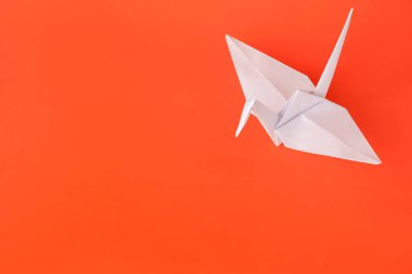 Origami art. Handmade paper crane on orange background, above view. Space for text