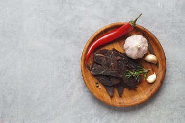 Plate with pieces of delicious beef jerky and spices on light grey table, top view. Space for text